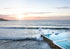 Ocean waves crashing against a wall with a sunset over the water.