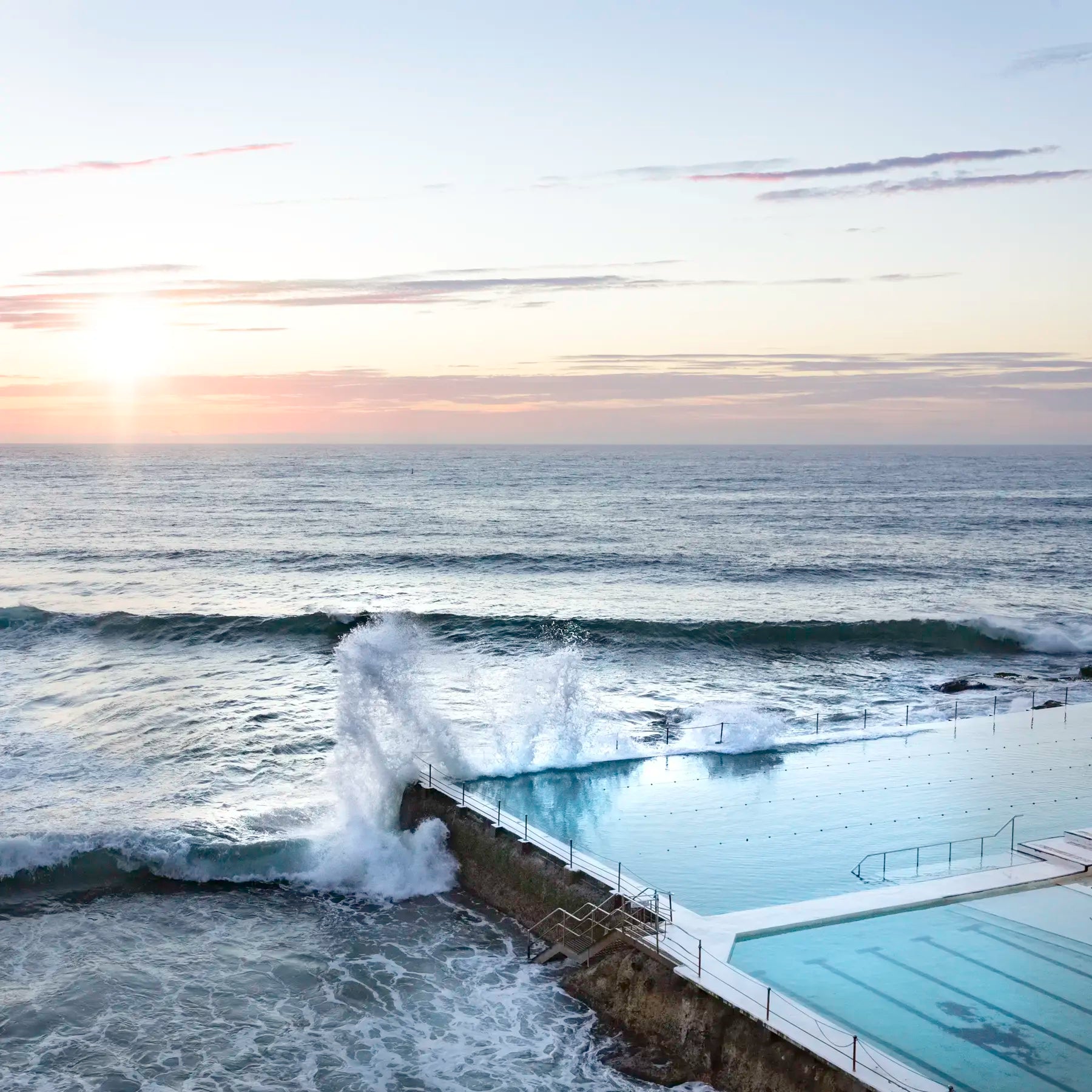 Ocean waves crashing against a rocky breakwater with a sunset sky.