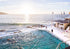 People swimming in an oceanside pool with ocean view and lifeguard tower.