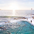People swimming in an ocean pool with a view of the sea and sky.