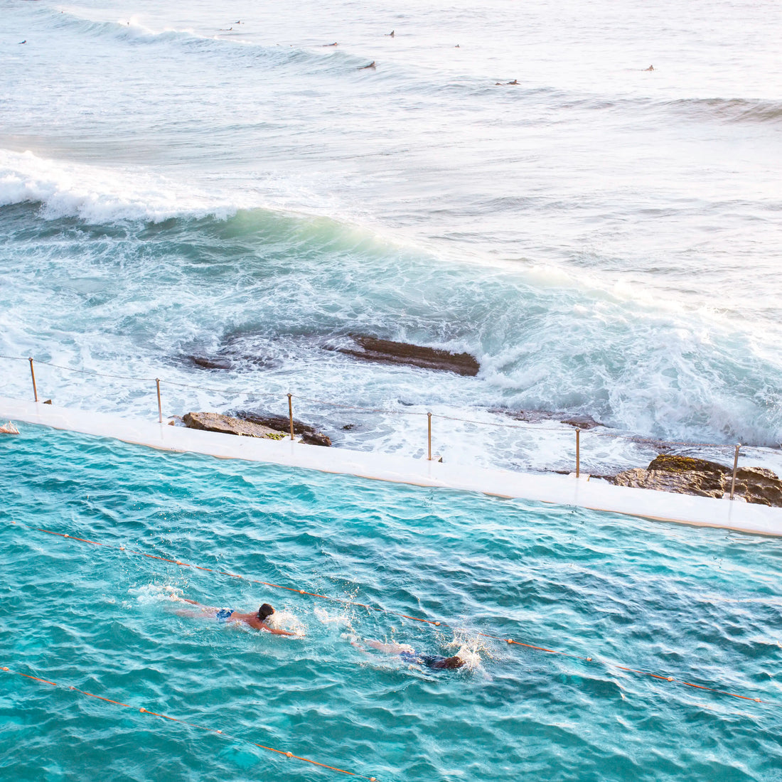 Two people swimming in the Bondi iceberg ocean pool with ocean waves in the background