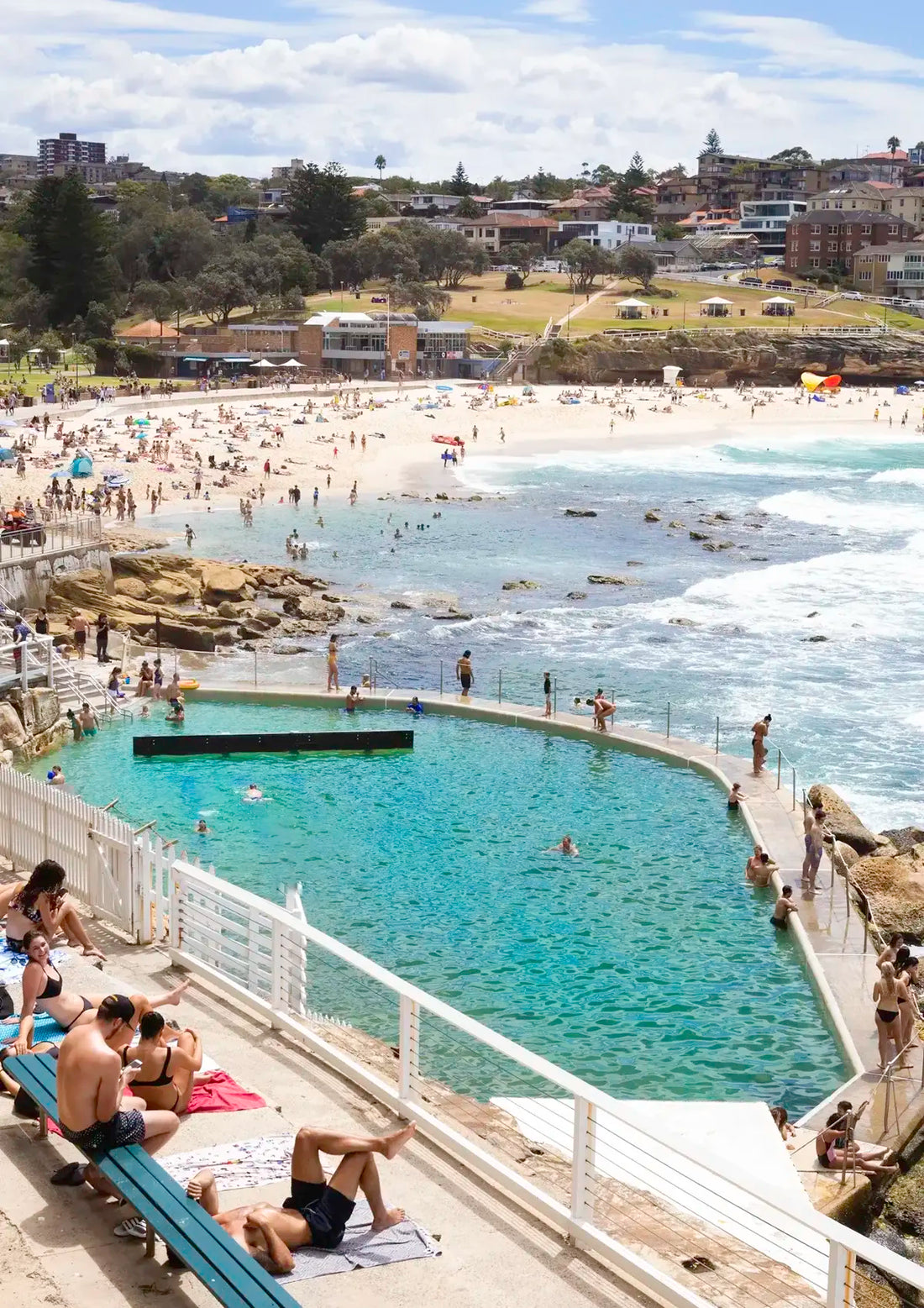 People enjoying a beachside pool with a view of the ocean and coastal town.