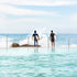 Two surfers with their boards standing in shallow water near rocks.