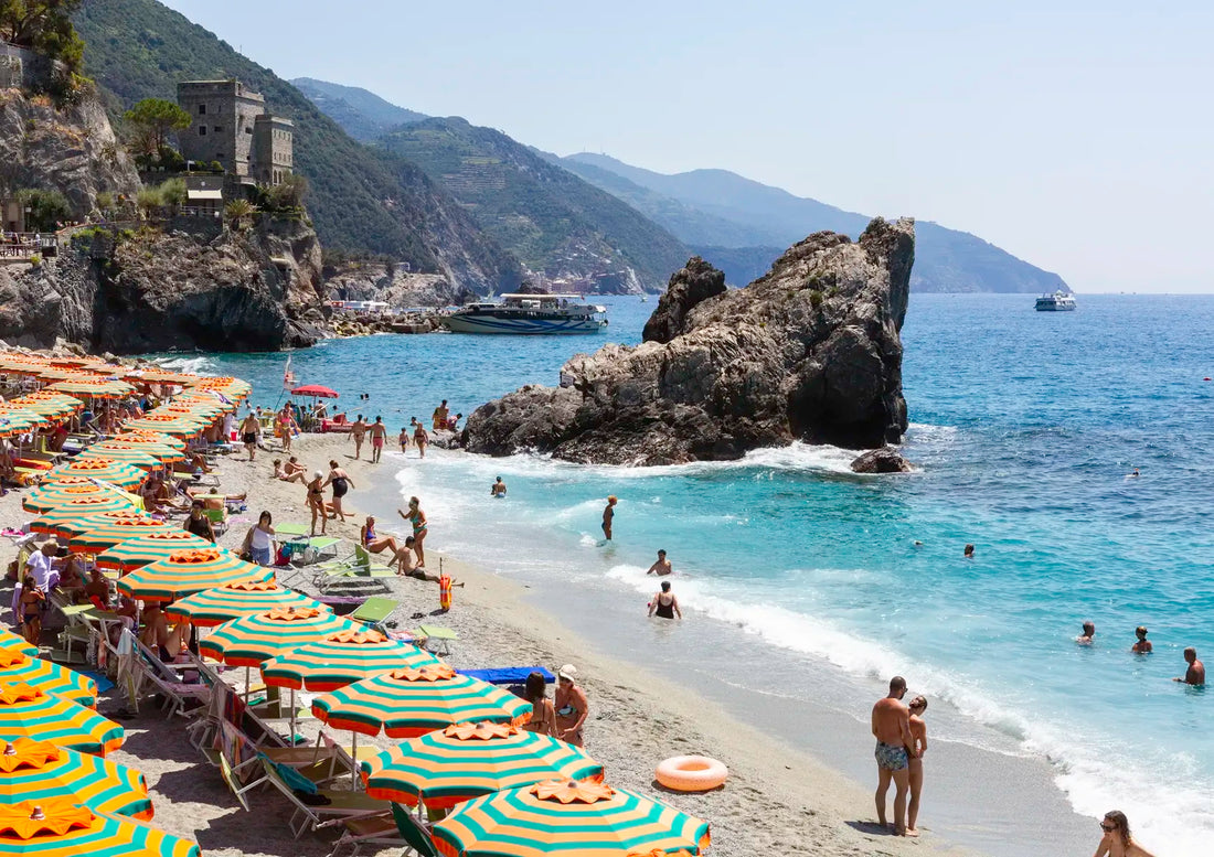 Beach scene with people, umbrellas, and mountains in the background