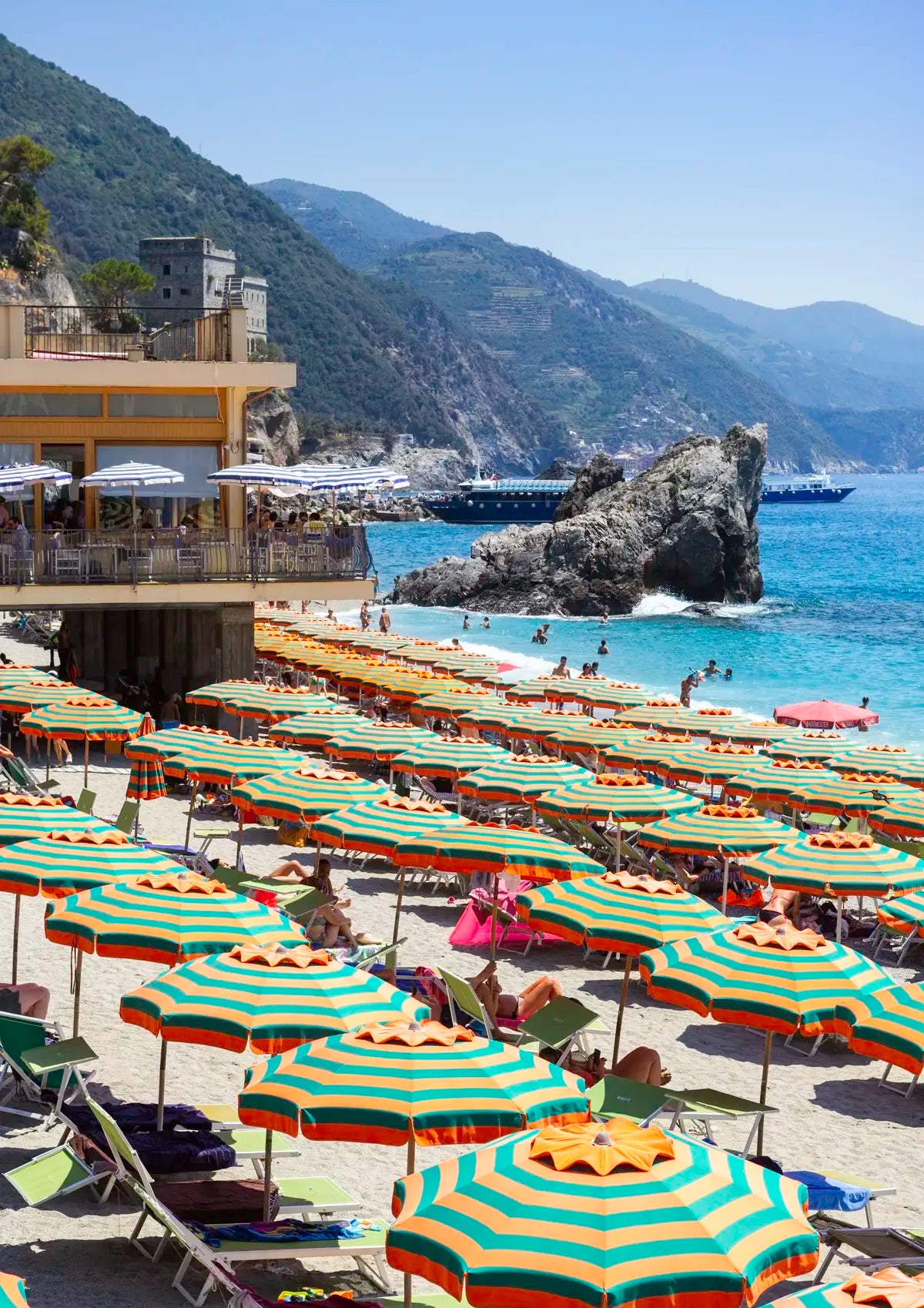 Beach with rows of striped umbrellas and a scenic view of mountains and sea.