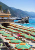 Beach with rows of striped umbrellas and a scenic view of mountains and sea.