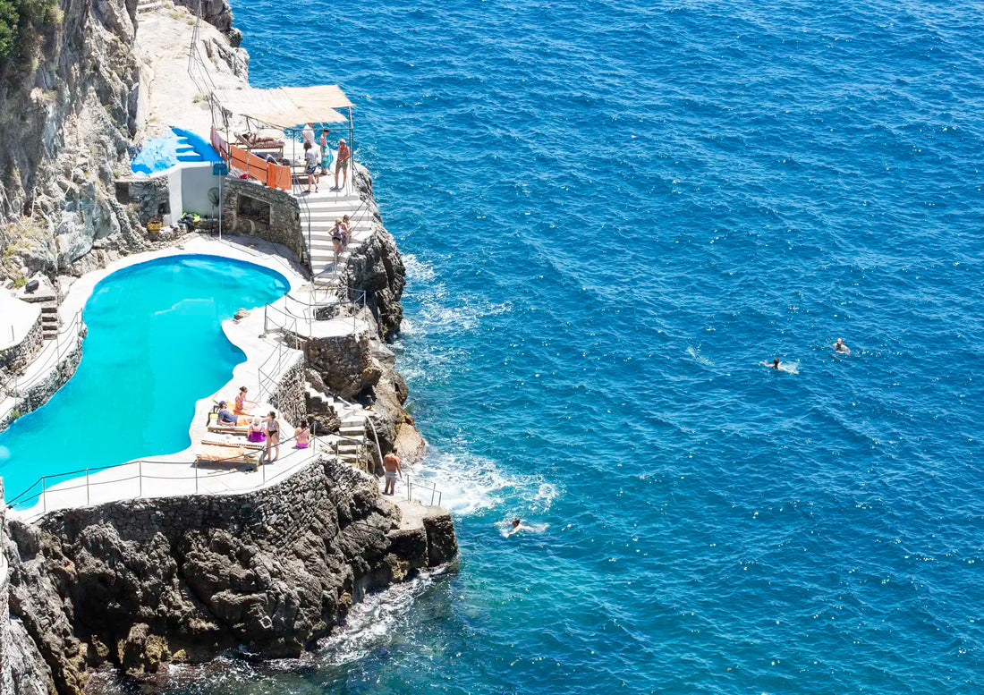 Crescent-shaped pool built into a cliffside with people enjoying the view over the ocean.