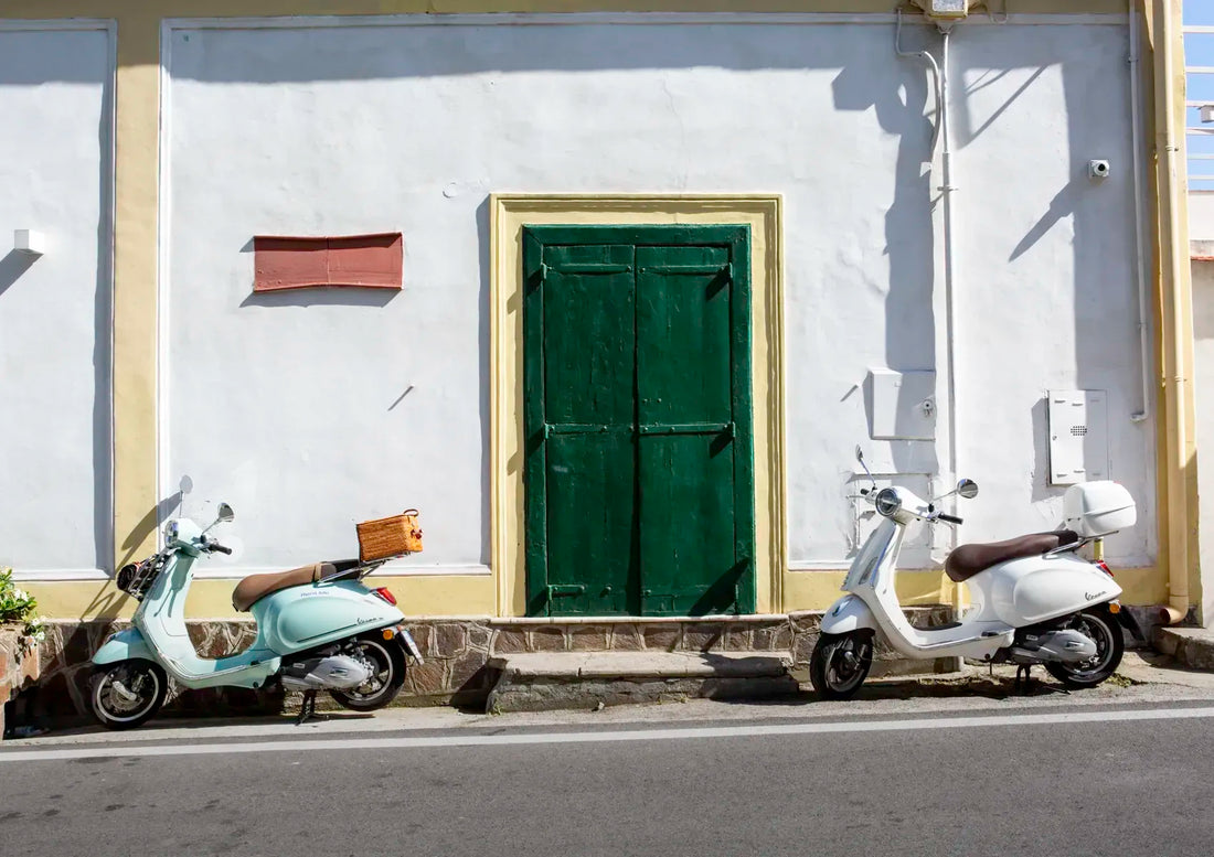 Two scooters parked on a street in front of a white wall with a green door.