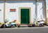 Two scooters parked on a street in front of a white wall with a green door.
