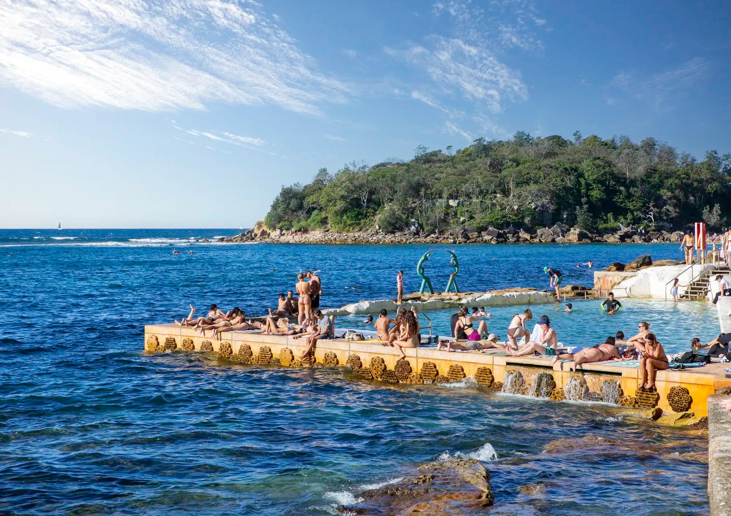 People enjoying the water at a natural pool by the sea with a scenic background.