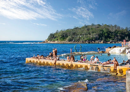 People enjoying the water at a natural pool by the sea with a scenic background.