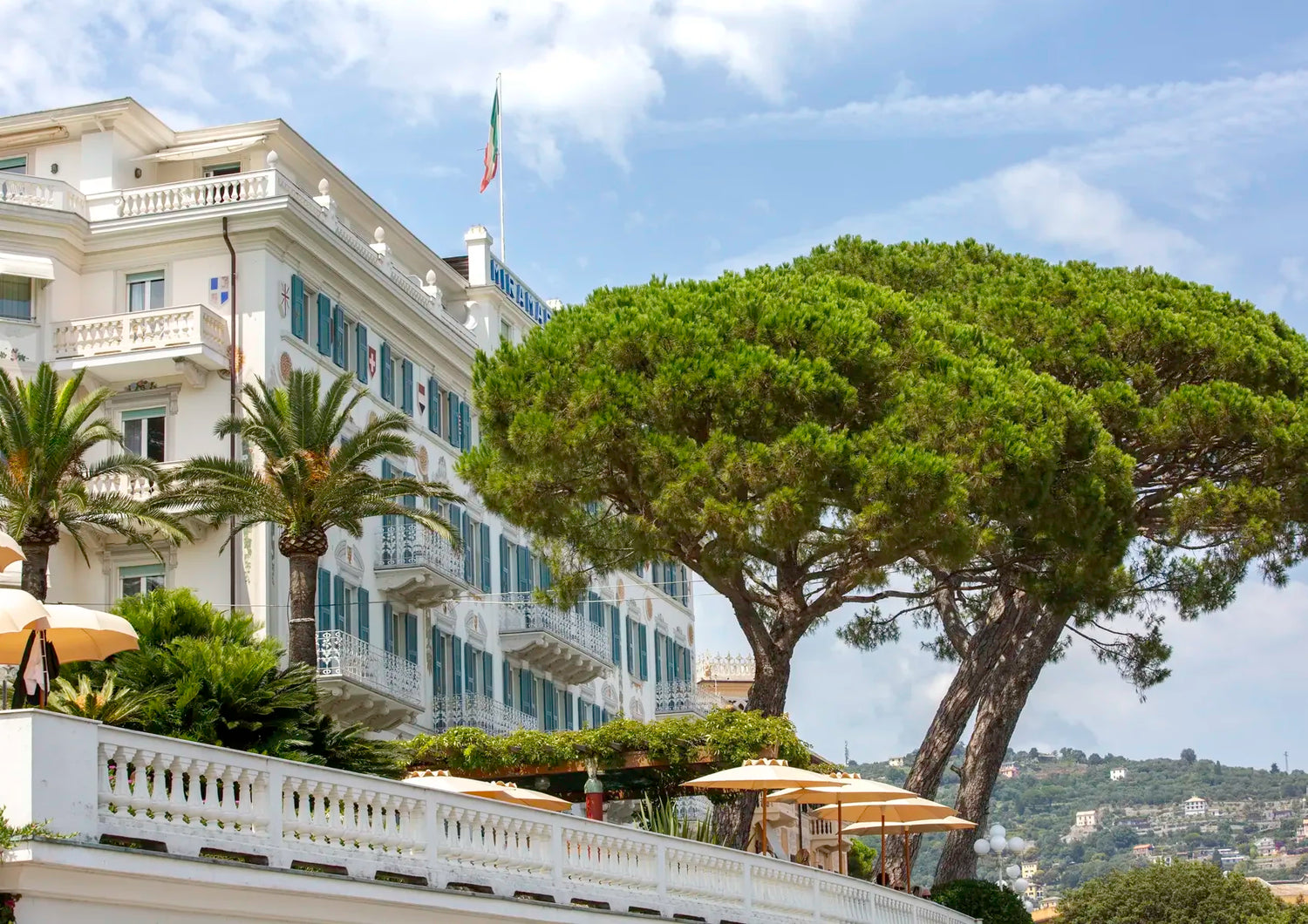 White building with balconies, trees, and umbrellas on a clear day.