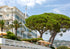 White building with balconies, trees, and umbrellas on a clear day.