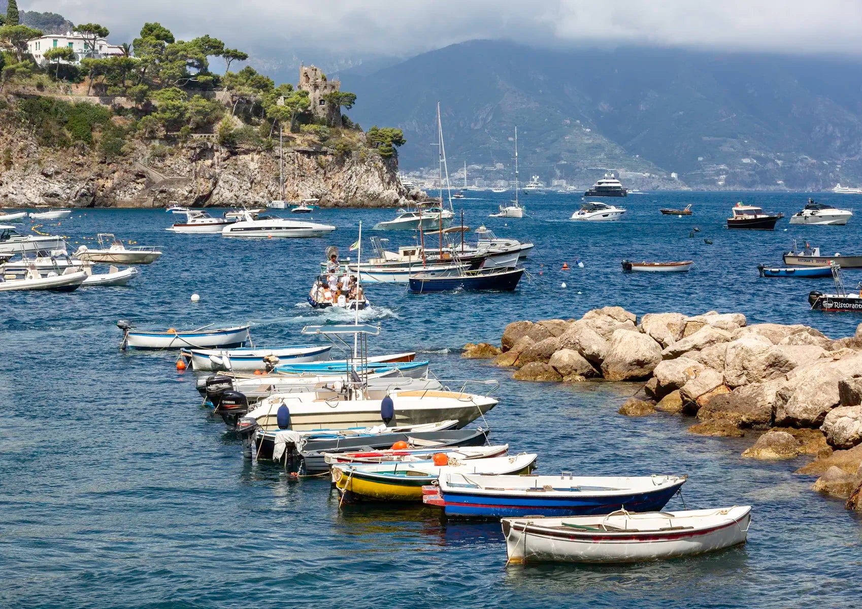 Boats docked in a harbor with rocky outcrops and mountains in the background