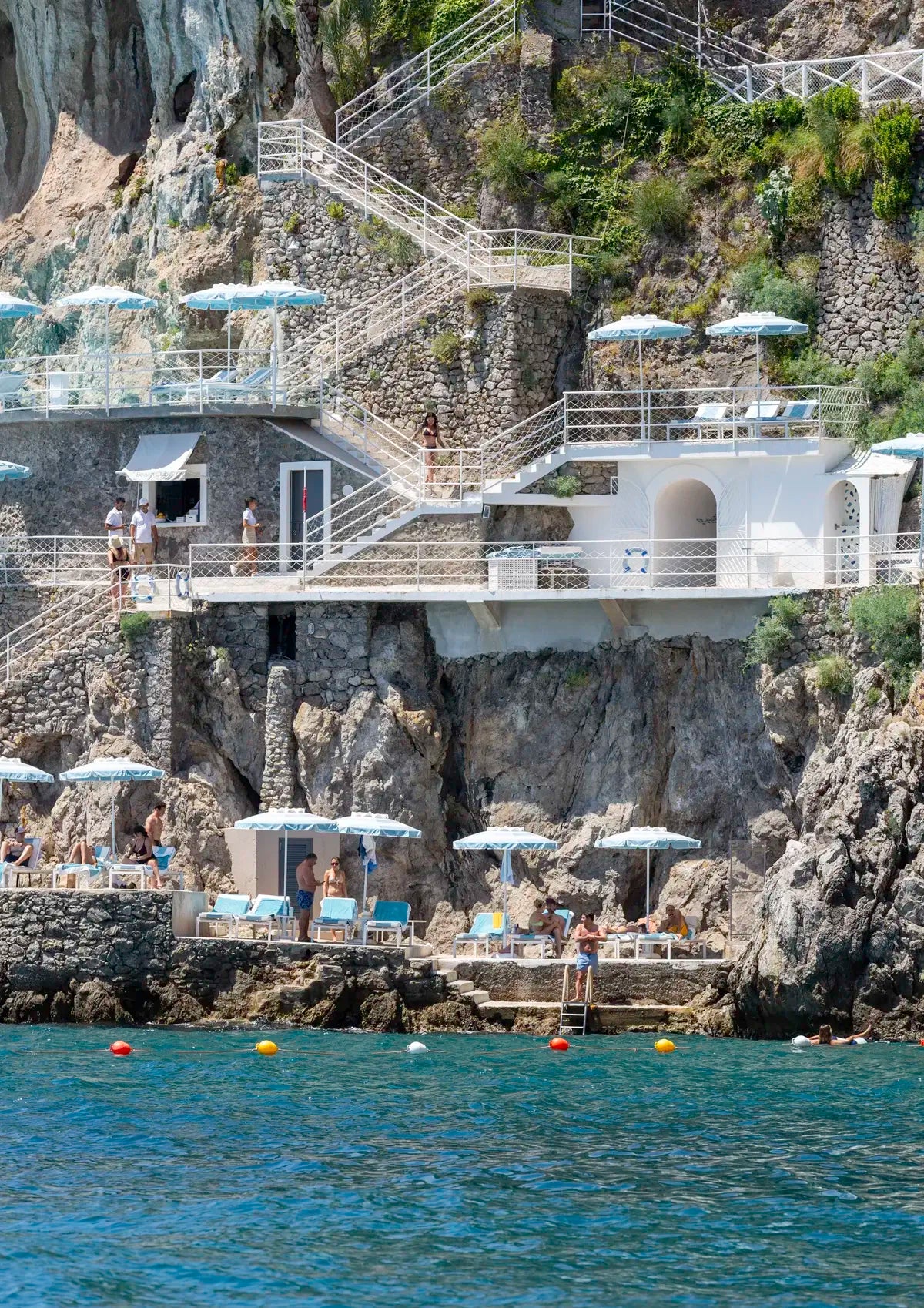 Staircase leading down to a cliffside with lounge chairs and umbrellas overlooking the ocean.
