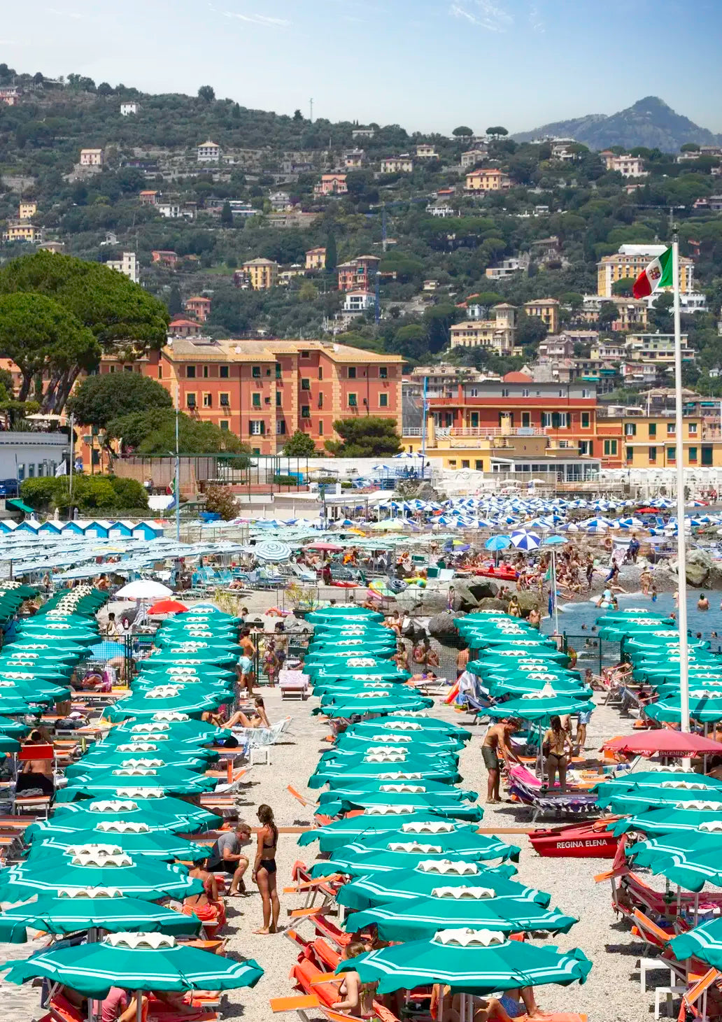 Beach scene with numerous green umbrellas and people in a coastal town setting.