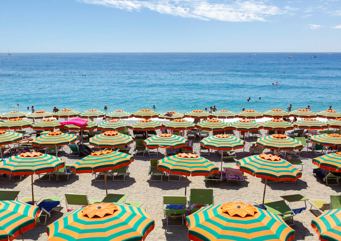 Beach scene with colorful umbrellas and people near the ocean under a clear blue sky.