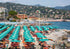 Beach scene with rows of umbrellas and chairs, buildings, and mountains in the background.
