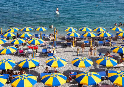 Beach scene with numerous blue and yellow umbrellas on a pebble beach.