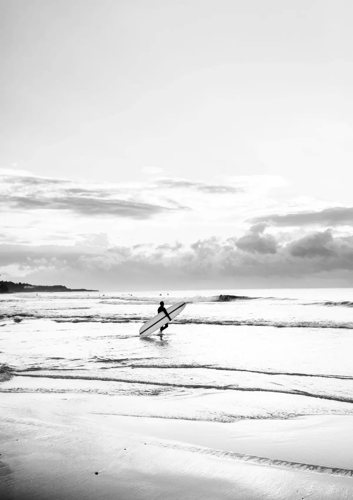 Person holding a surfboard walking out to surf with a cloudy sky