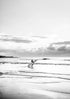 Person holding a surfboard walking out to surf with a cloudy sky
