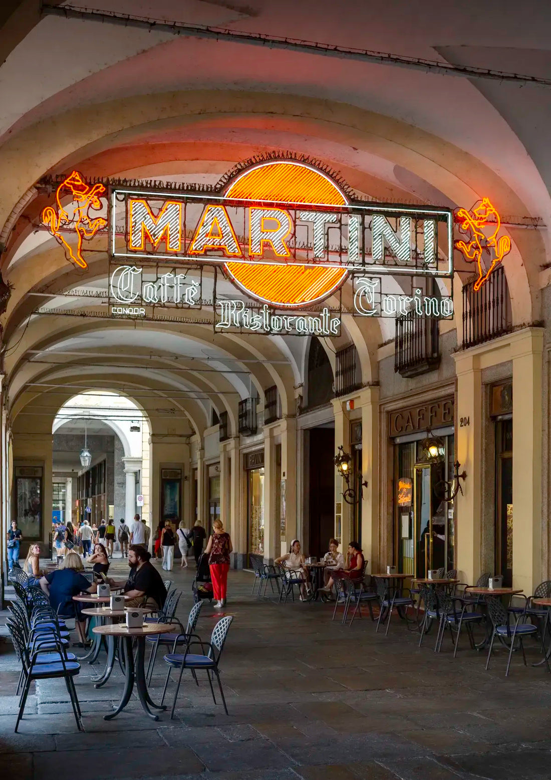 Neon Martini sign above a row of tables and chairs in an outdoor arcade.