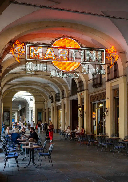 Neon Martini sign above a row of tables and chairs in an outdoor arcade.