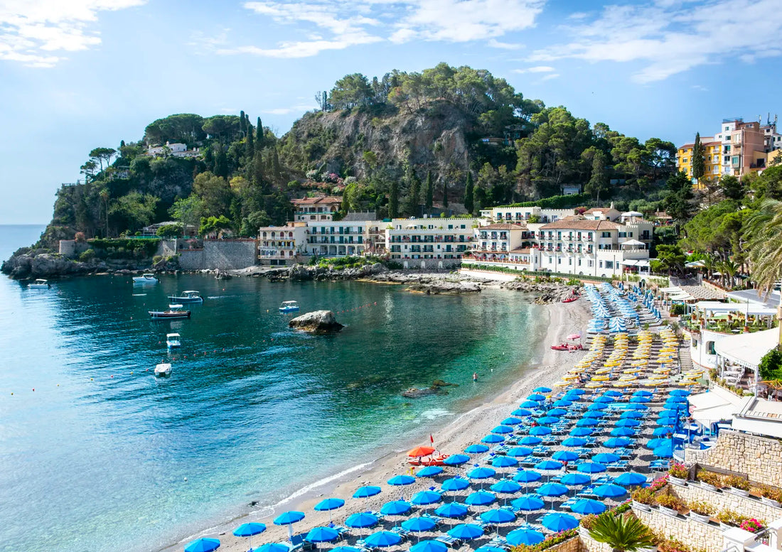 Coastal scene with beach, buildings, and blue umbrellas in a Mediterranean setting
