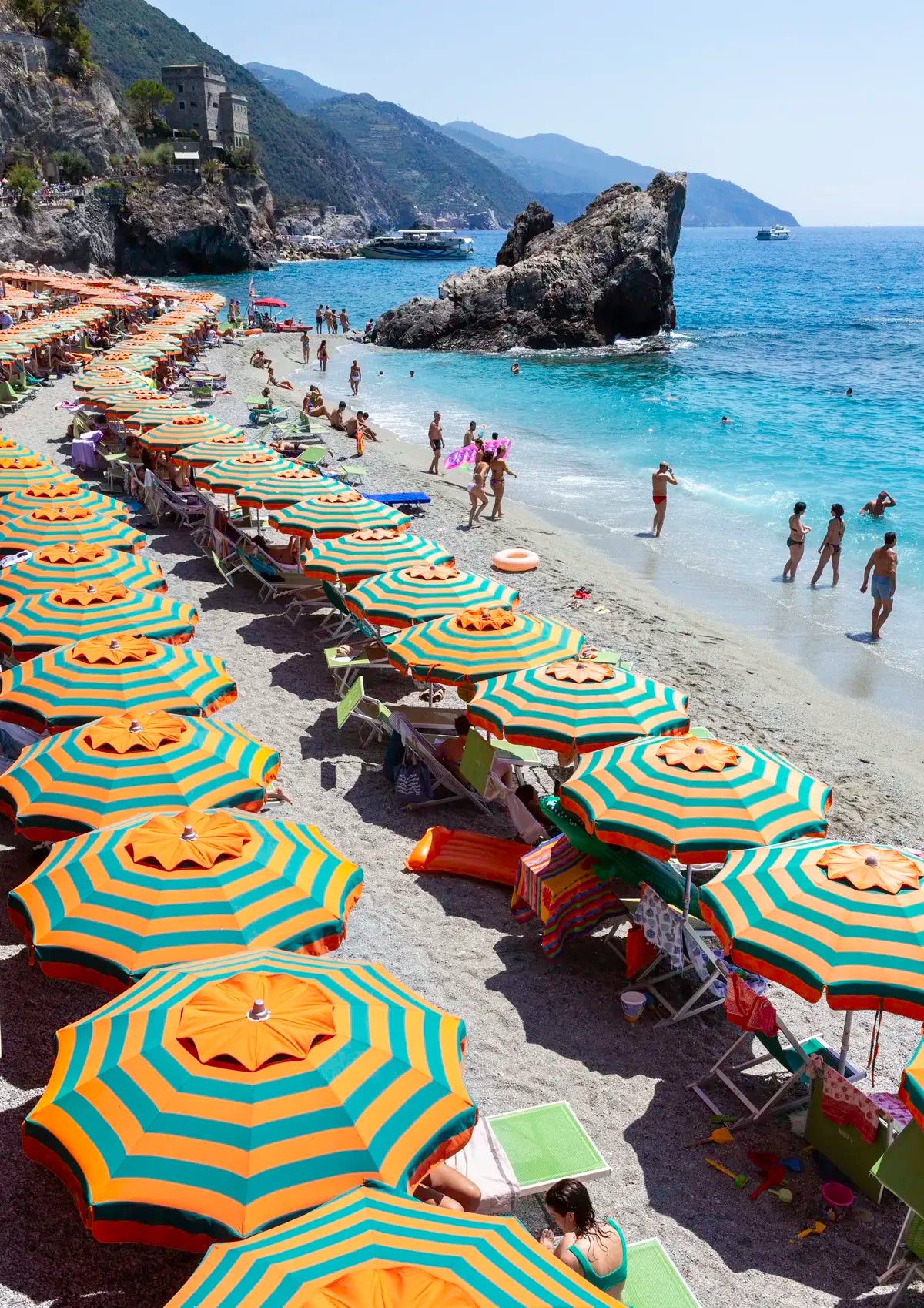 Beach scene with rows of yellow and blue striped umbrellas, people, and mountains in the background.
