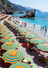 Beach scene with rows of yellow and blue striped umbrellas, people, and mountains in the background.