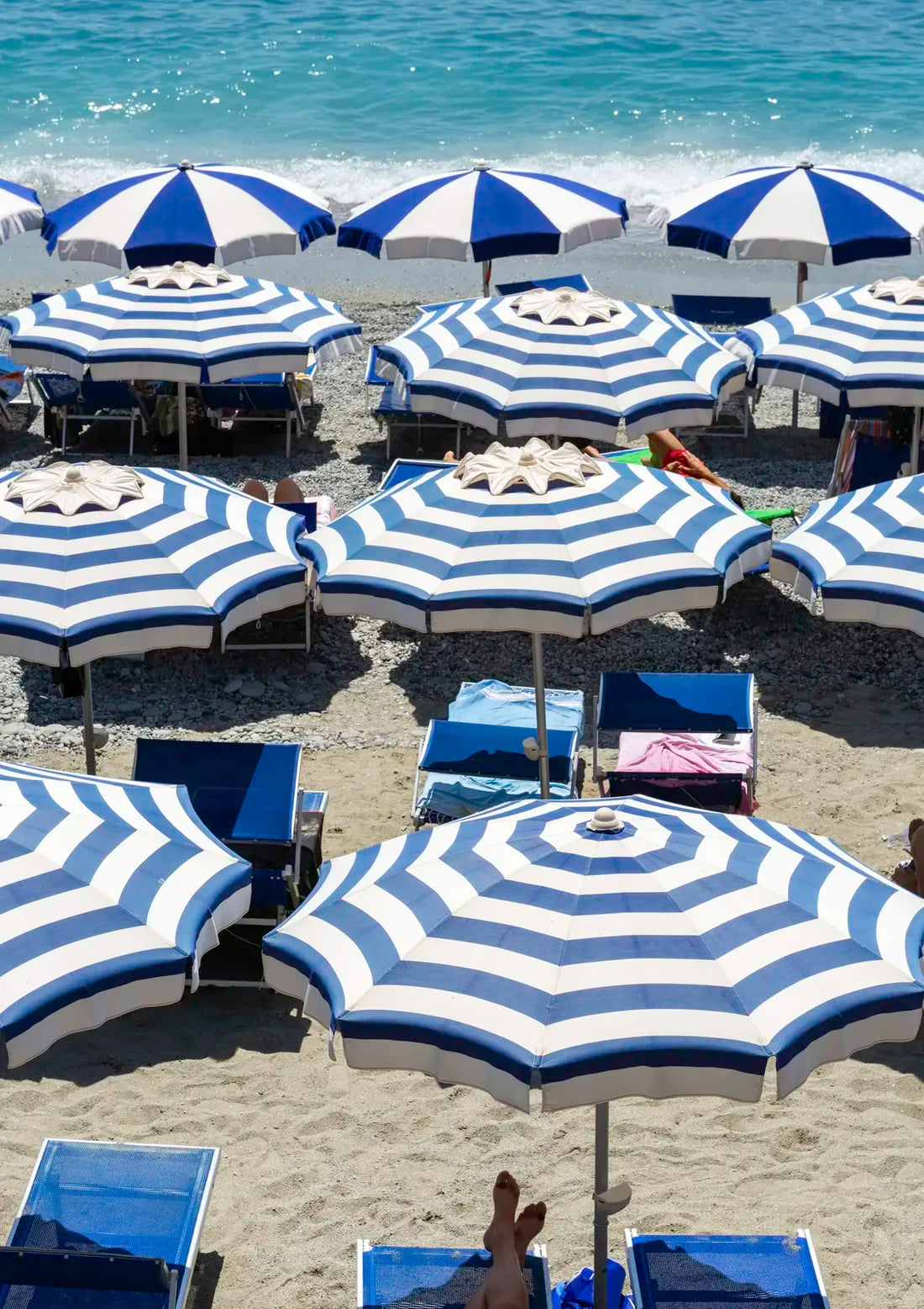 Beach scene with blue and white striped umbrellas and lounge chairs on a sandy beach.