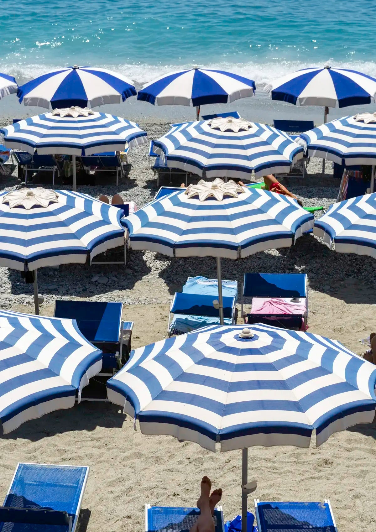 Beach scene with blue and white striped umbrellas and lounge chairs on a sandy beach.