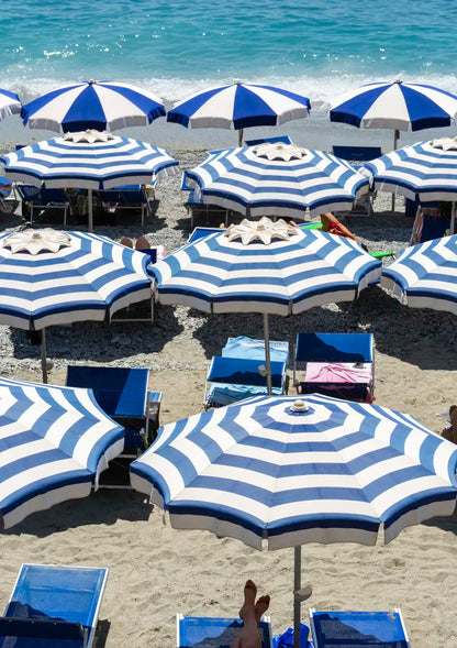 Beach scene with blue and white striped umbrellas and lounge chairs on a sandy beach.
