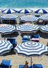 Beach scene with blue and white striped umbrellas and lounge chairs on a sandy beach.