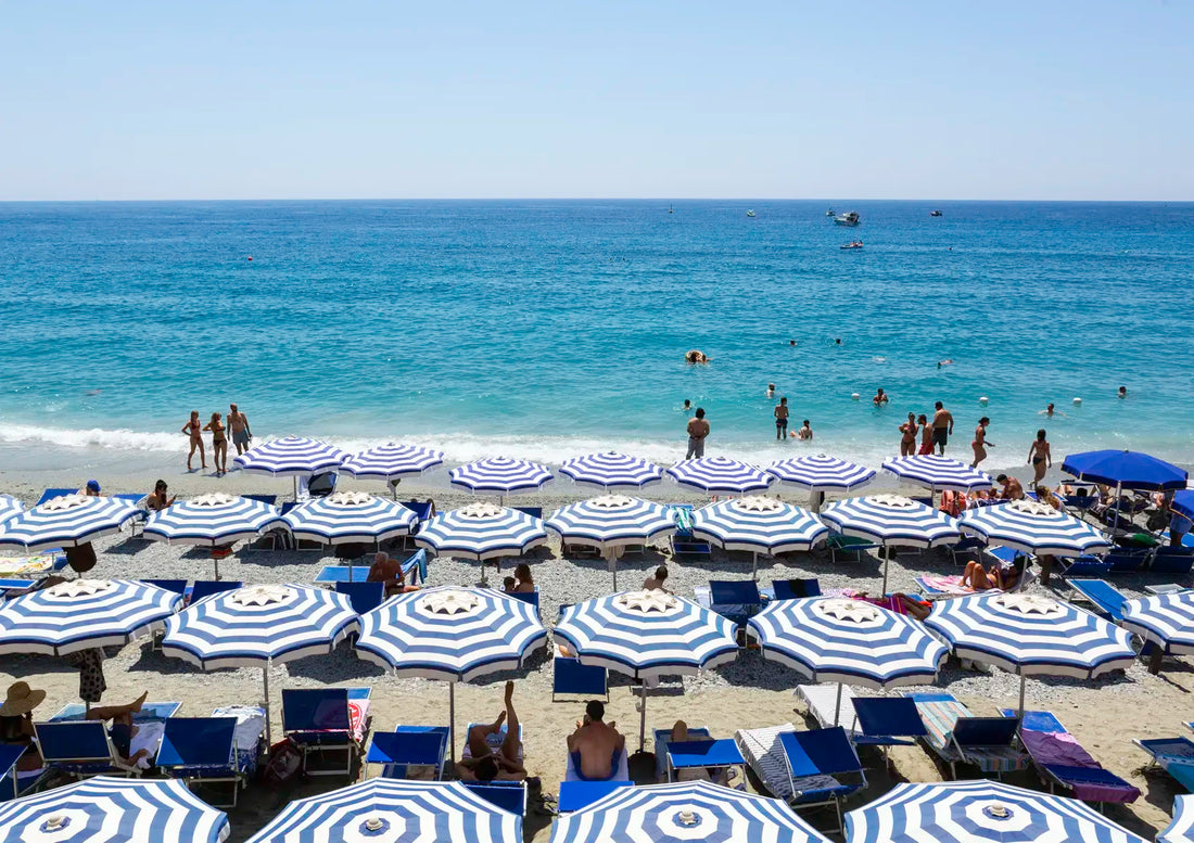 Beach scene with blue and white striped umbrellas and people enjoying the sun and water.