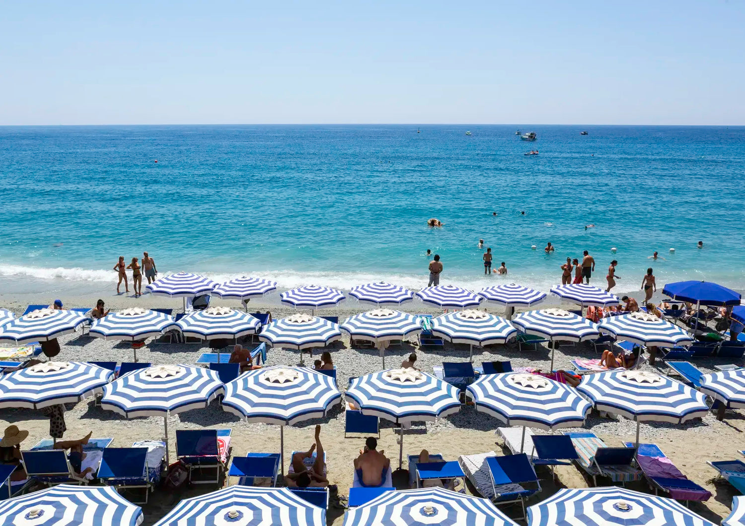 Beach scene with blue and white striped umbrellas and people enjoying the sun and water.