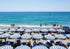 Beach scene with blue and white striped umbrellas and people enjoying the sun and water.