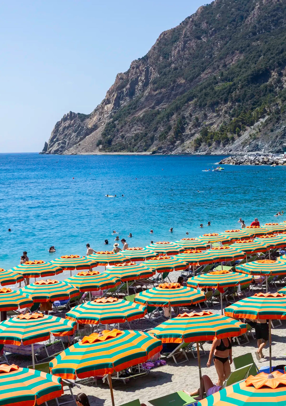 Beach scene with striped umbrellas, blue water, and mountains in the background