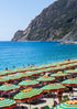 Beach scene with striped umbrellas, blue water, and mountains in the background