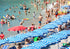 Beach scene with people swimming and sunbathing under blue and white striped umbrellas.