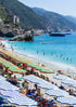 Beach scene with striped umbrellas, people, and boats near a mountainous coastline.