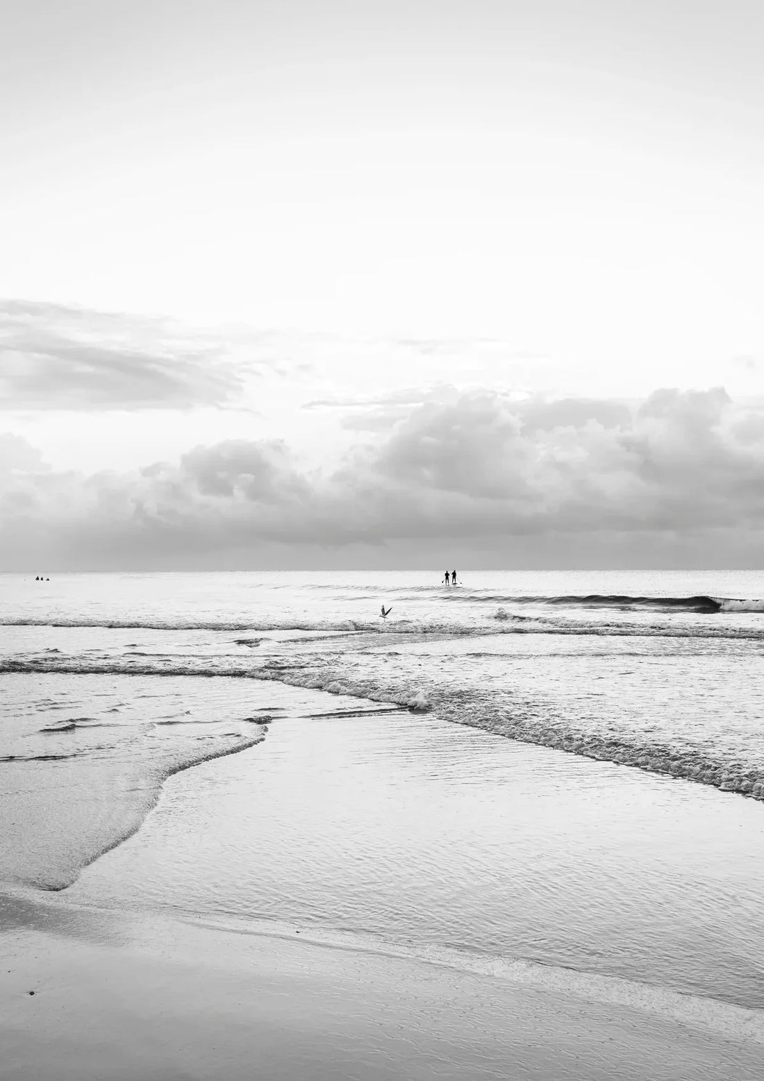 Black and white beach scene with people walking on the horizon under a cloudy sky.