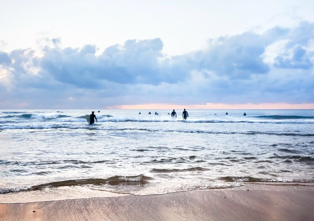 Surfers making there way into the ocean with a cloudy sky