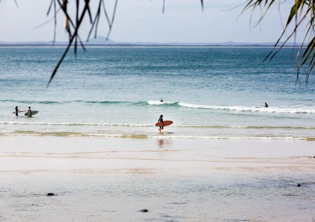 Surfers on a beach with calm ocean and distant land.