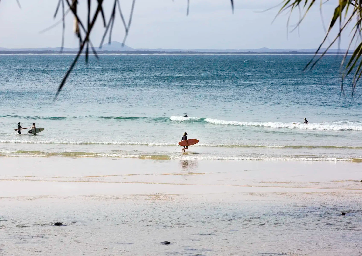 Surfers on a beach with calm ocean and distant land.