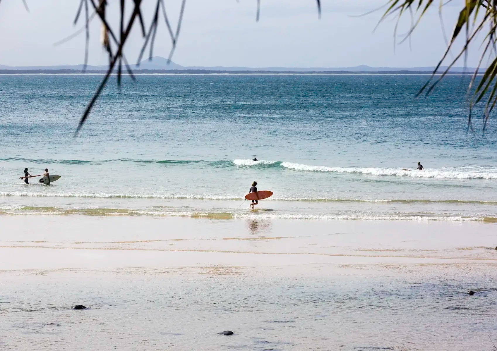 Surfers on a beach with calm ocean and distant land.