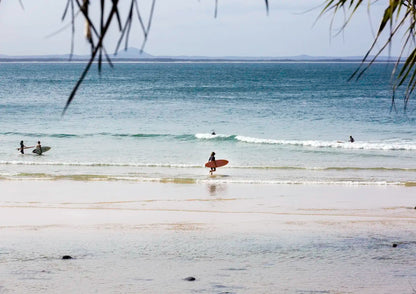 Surfers on a beach with calm ocean and distant land.