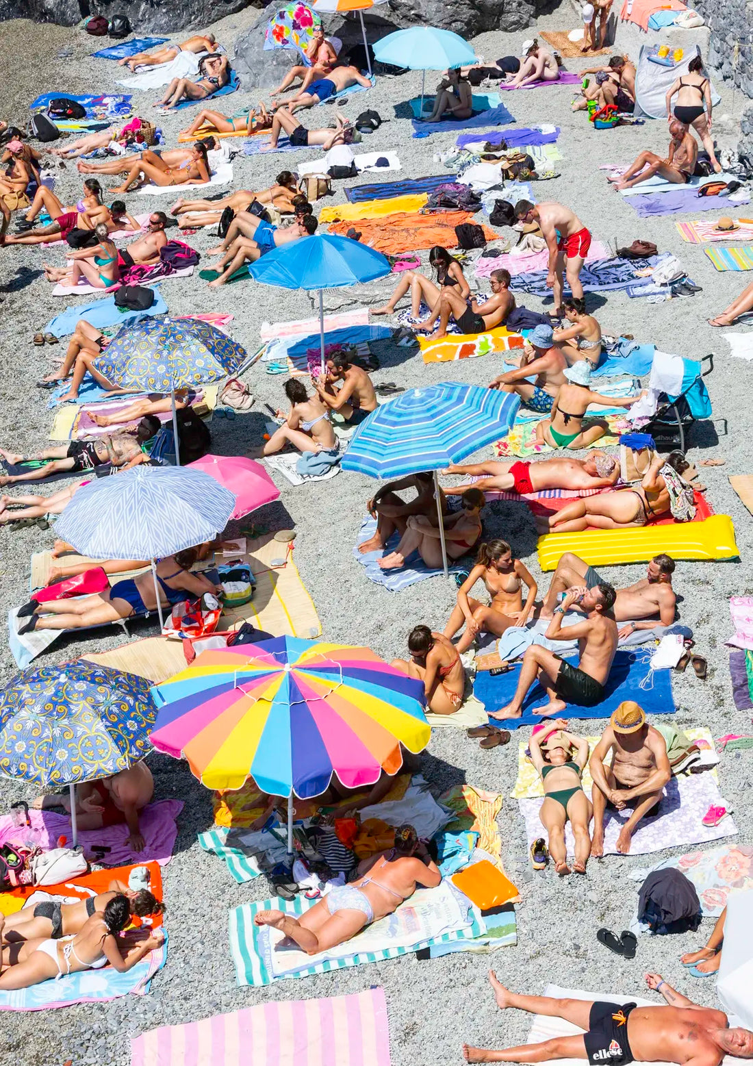 People sunbathing on a crowded beach with colorful umbrellas and towels.