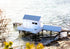 Small white boatshed on stilts by a body of water with a dock.