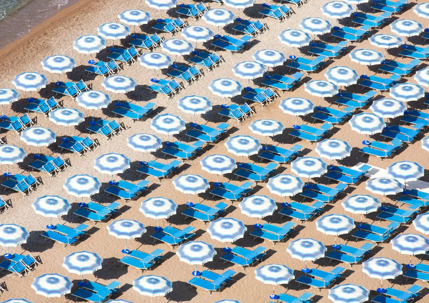 Pattern of blue and white umbrellas and lounge chairs on a sandy beach.